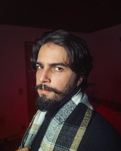 Free A stylish bearded man with a plaid scarf poses indoors, showcasing modern fashion. Stock Photo