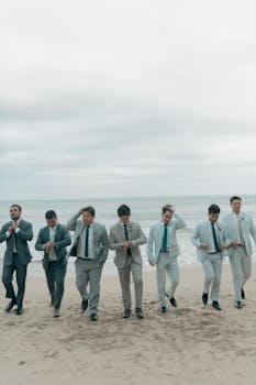 Seven groomsmen in suits walking along a beach, showcasing stylish wedding attire.