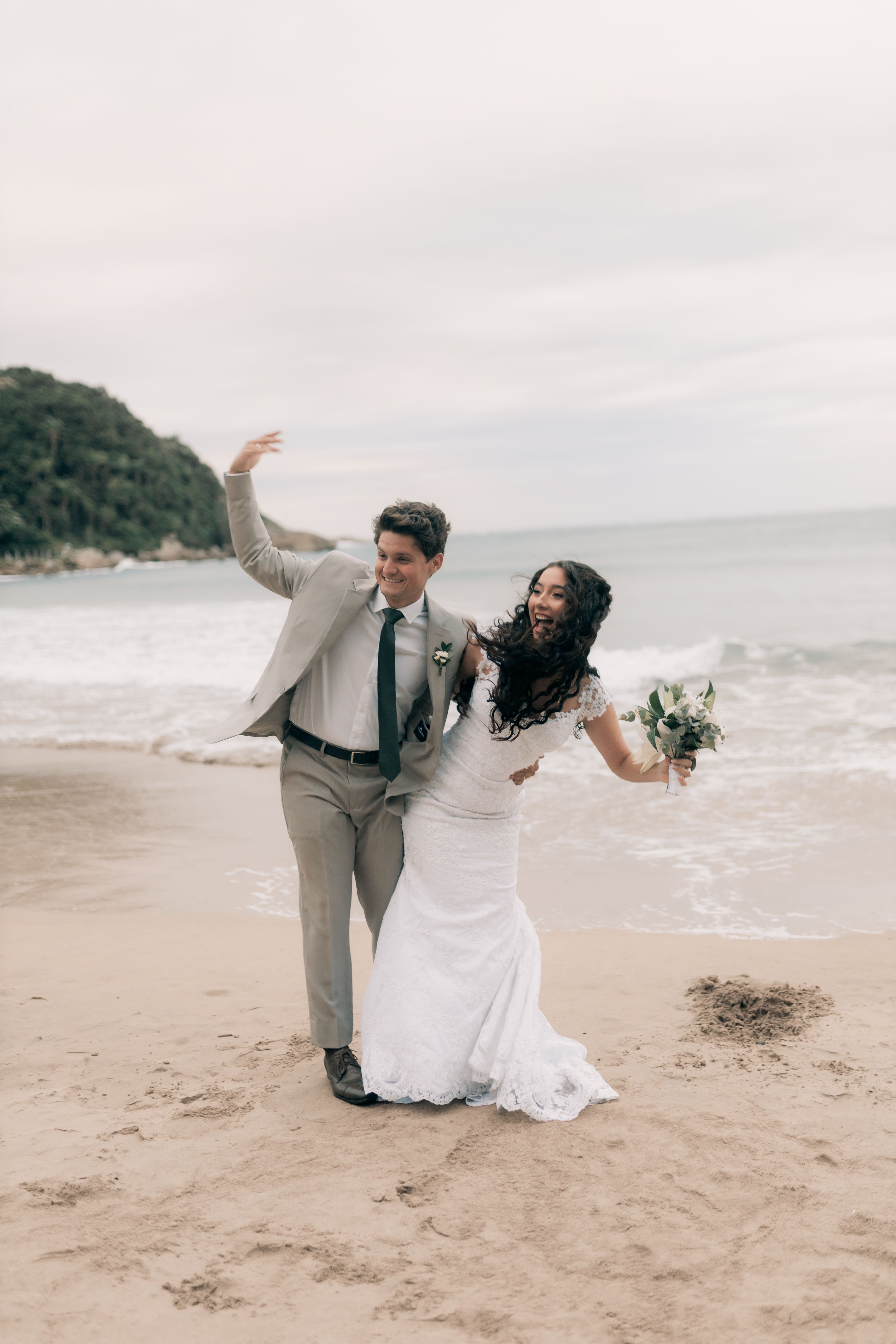 Happy couple in wedding attire celebrating on a scenic beach location.