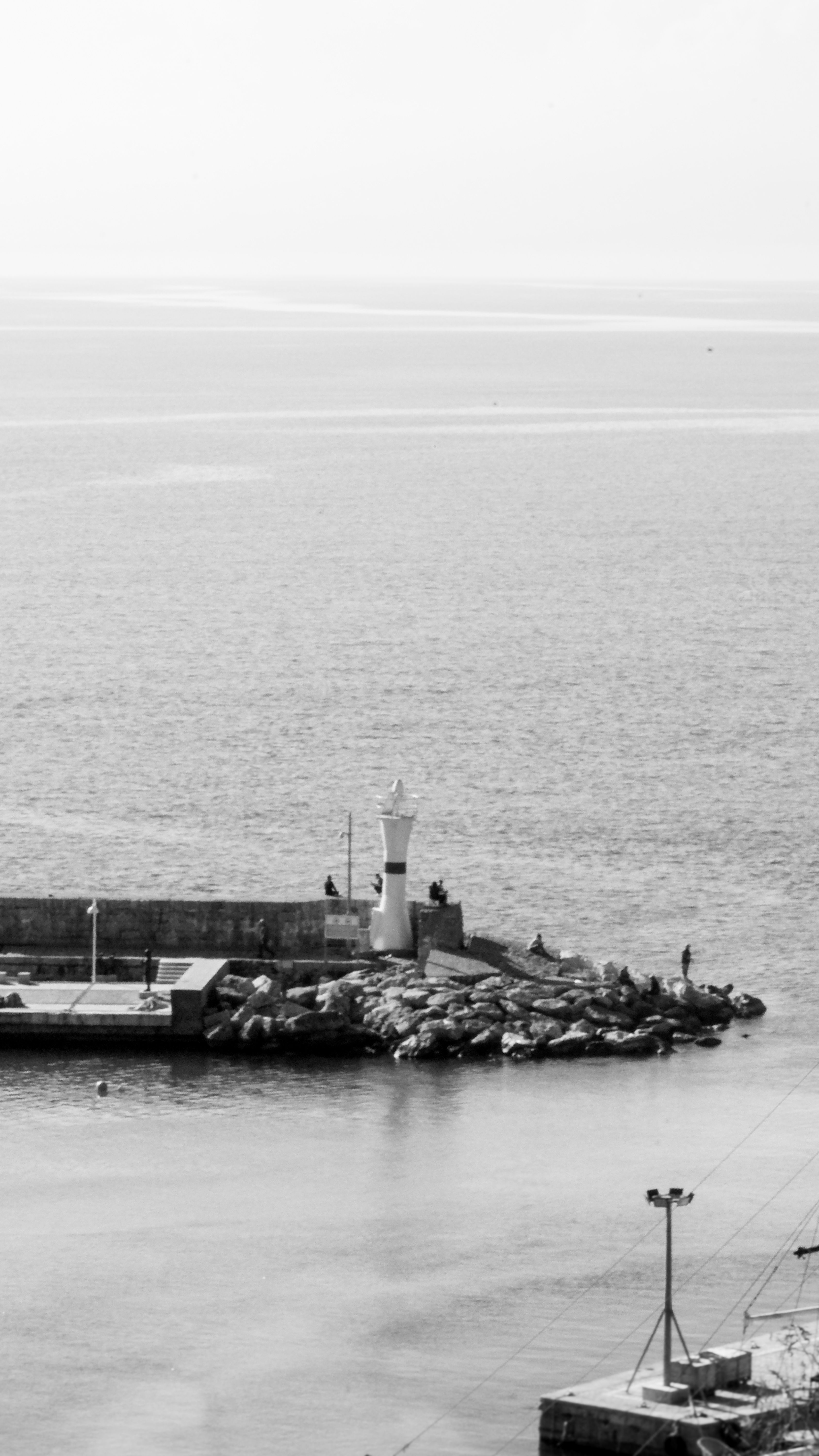 A black and white photograph of a lighthouse on a pier by the sea, capturing solitude and calmness.