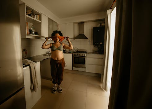 Woman in kitchen adjusting clothes, showcasing casual lifestyle in a modern kitchen environment.