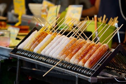 Close-up of assorted sausages on a grill at a bustling street food market.