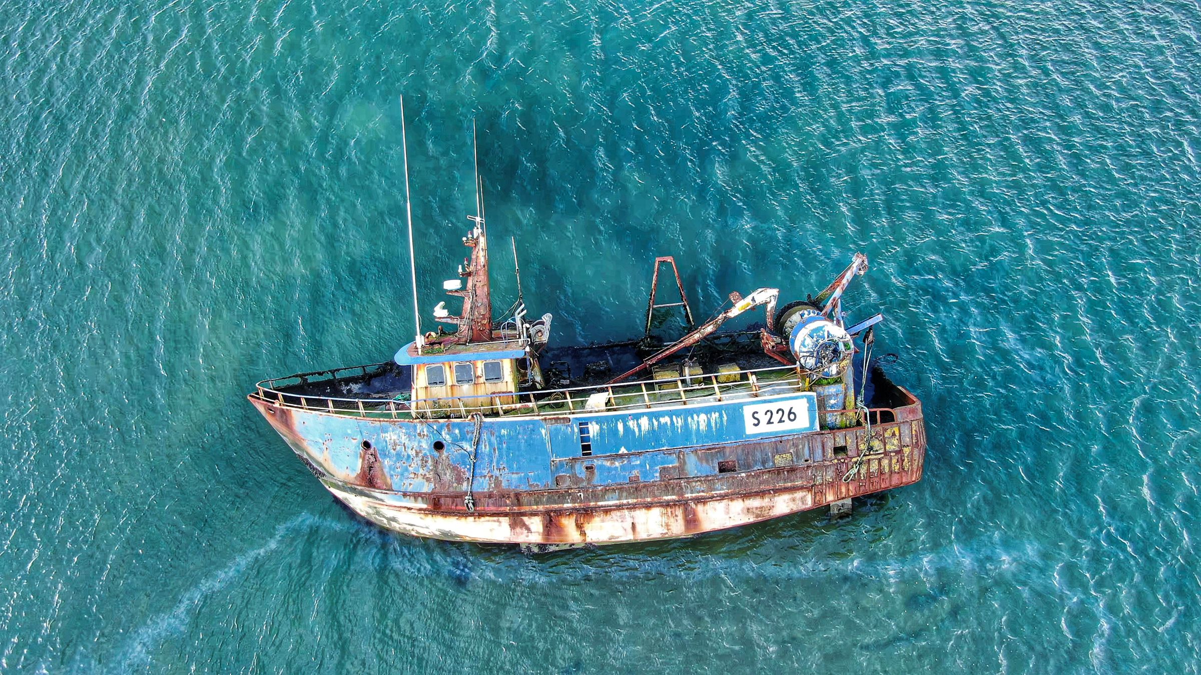 Drone shot of a rusty fishing boat in clear Irish waters