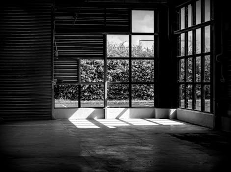 Moody black and white shot of an industrial warehouse interior with large windows.