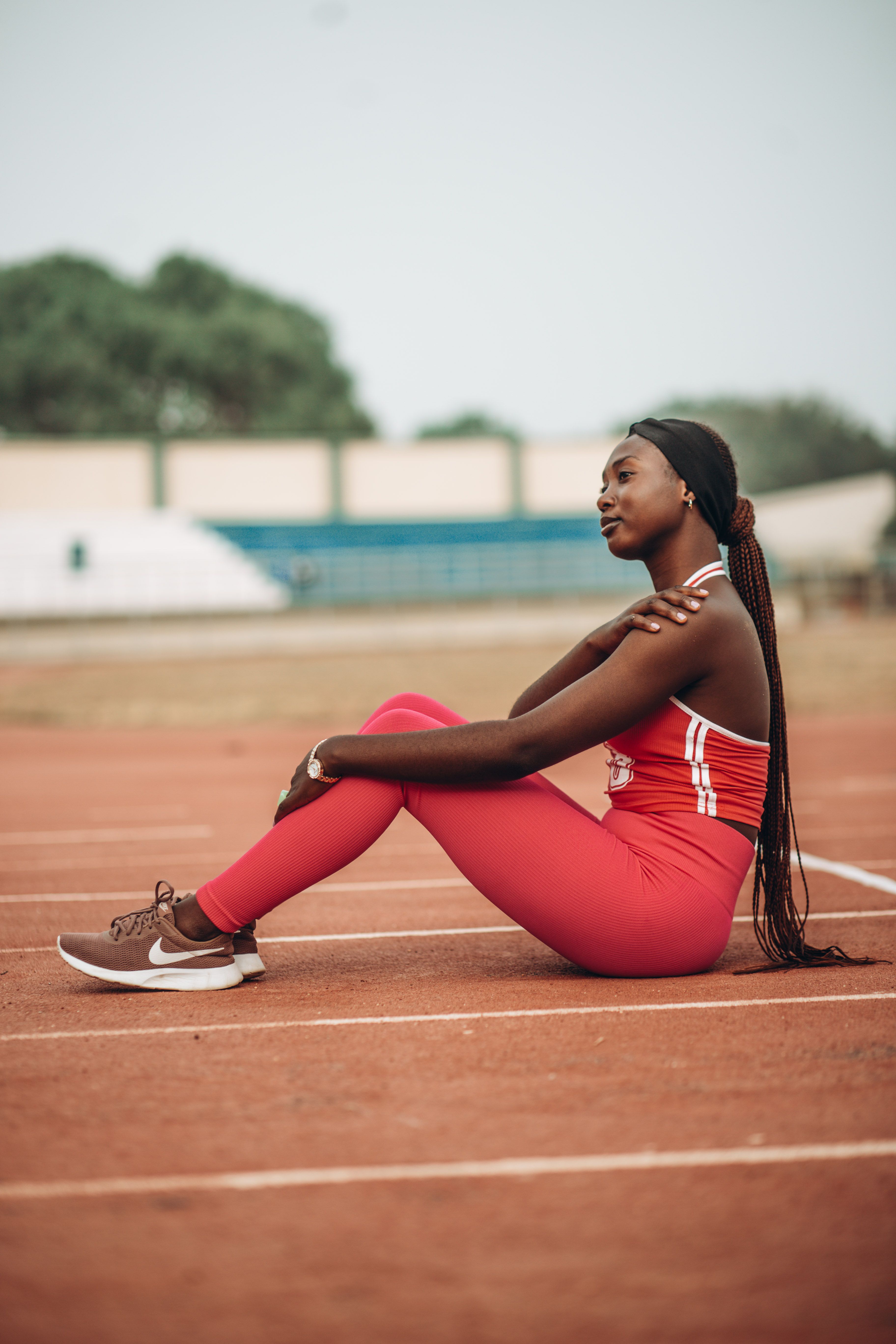 Young woman in red athletic wear resting on a track field outdoors.
