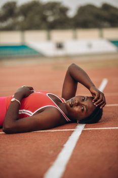 Woman in sportswear relaxing on a running track, showcasing stamina and fitness.