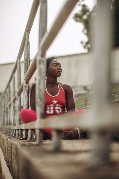 Free Young woman in red activewear meditating outdoors, promoting mindfulness and relaxation. Stock Photo