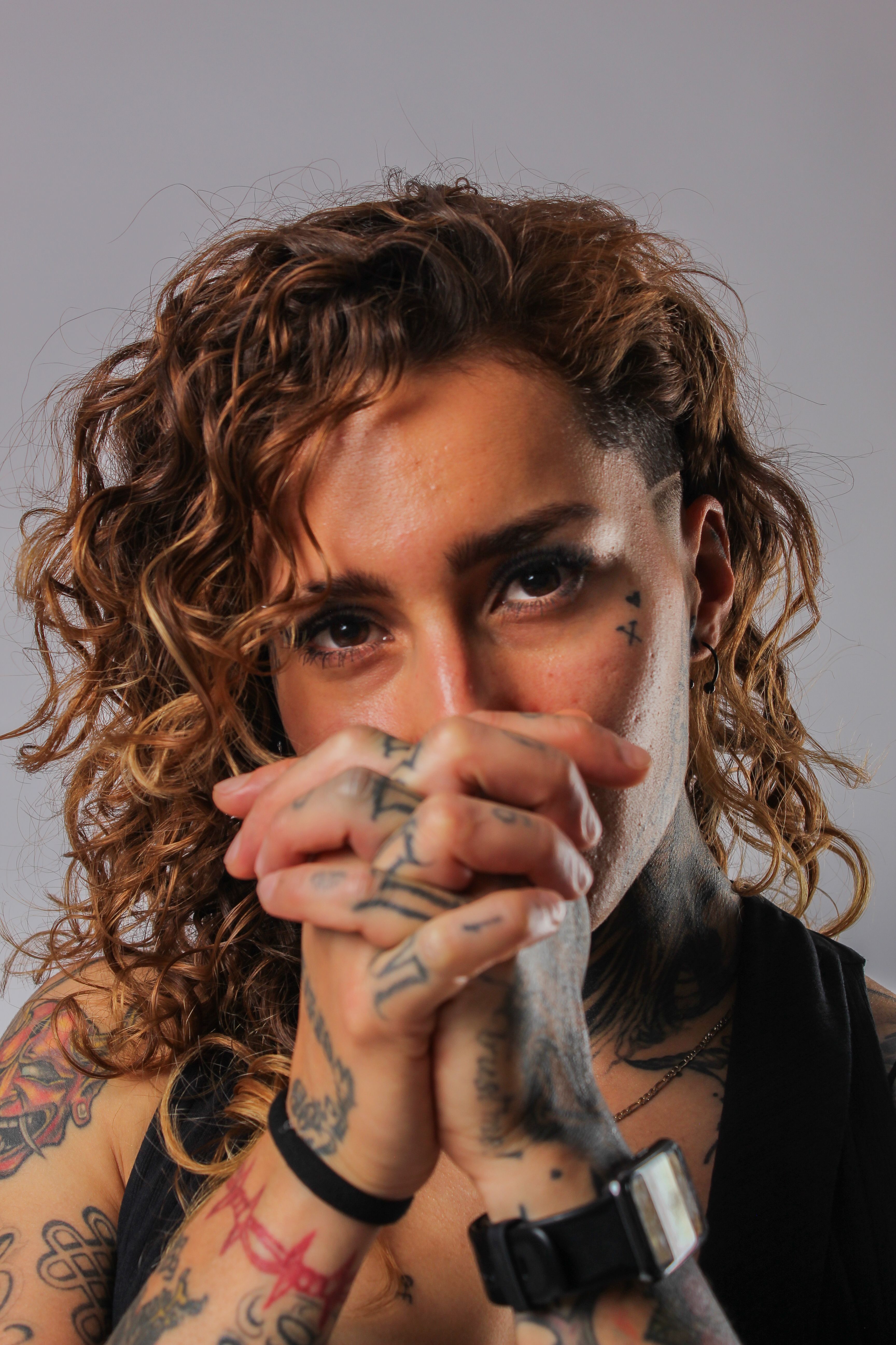 Close-up studio portrait of a tattooed woman with curly hair, expressing confidence.