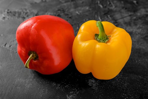 Free Close-up of vibrant red and yellow bell peppers on a textured dark surface, perfect for culinary themes. Stock Photo