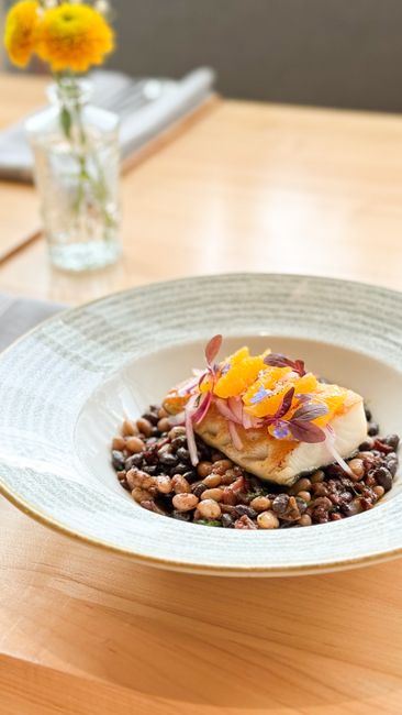 Two seared tilapia fillets on a bed of seasoned black beans, topped with cilantro and lime wedges in a dark skillet.