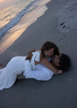 A couple in love embraces on a sandy beach at sunset, capturing a serene romantic moment.