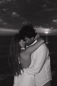 A couple embraces by the ocean at sunset, capturing love's tender moments.