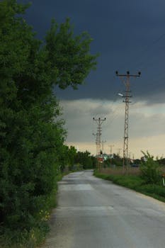 Empty rural road with power lines and dark clouds, suggesting an approaching storm.