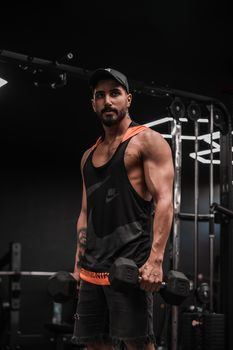 A muscular man in a gym lifting dumbbells intensely, showcasing strength.