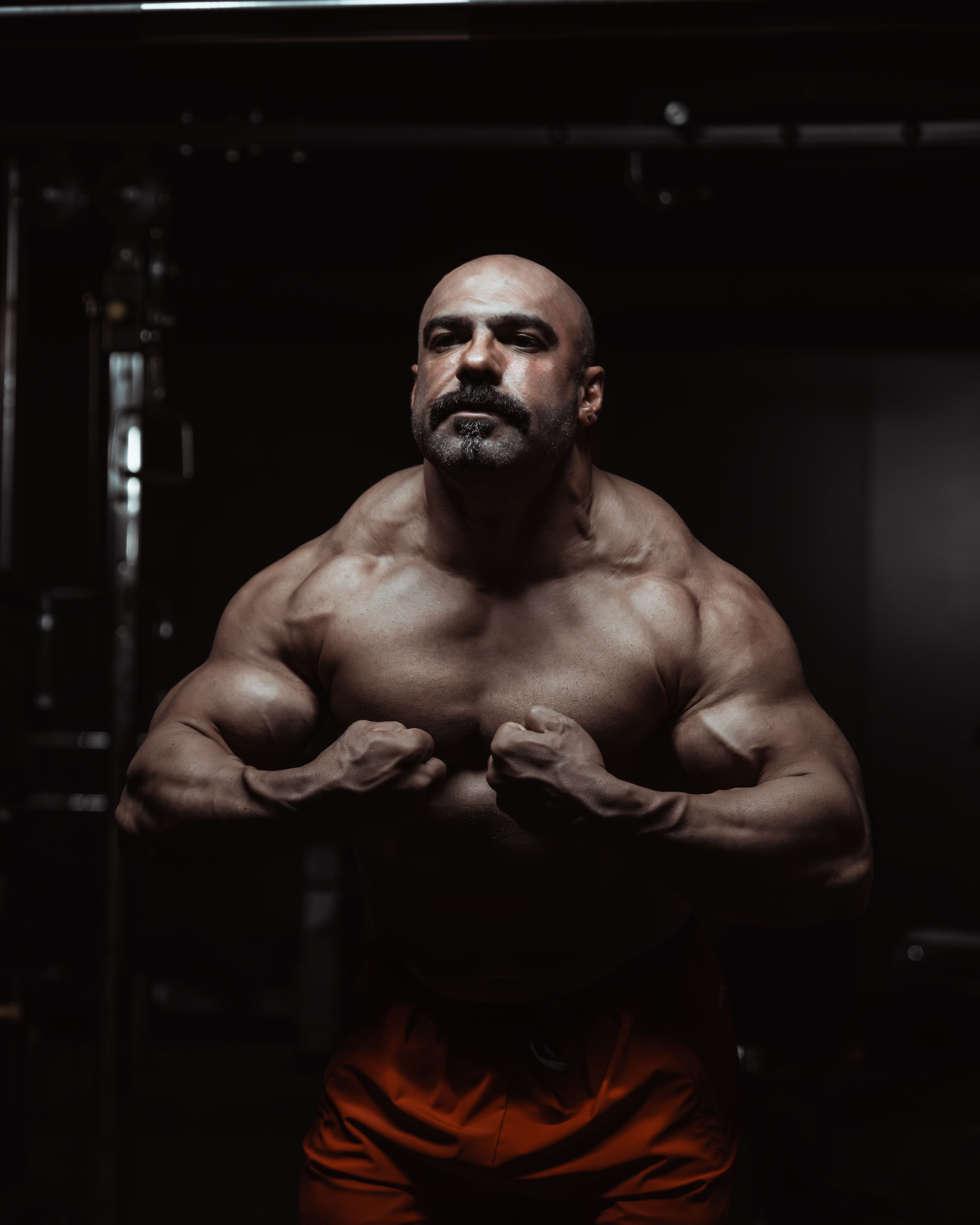 Strong male bodybuilder flexing muscles in low-light gym setting.
