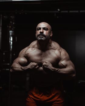 Strong male bodybuilder flexing muscles in low-light gym setting.