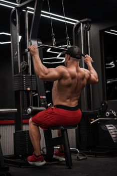 Strong man in gym performing lat pulldown exercise, highlighting muscle definition.