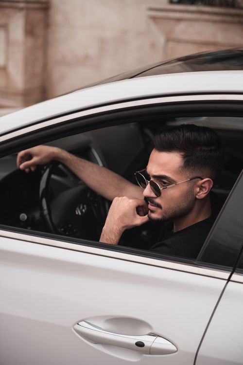 Free Young man with sunglasses driving a sleek car, exuding confidence and style. Stock Photo