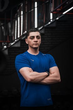 Portrait of a confident man in blue, standing in a gym setting with crossed arms.