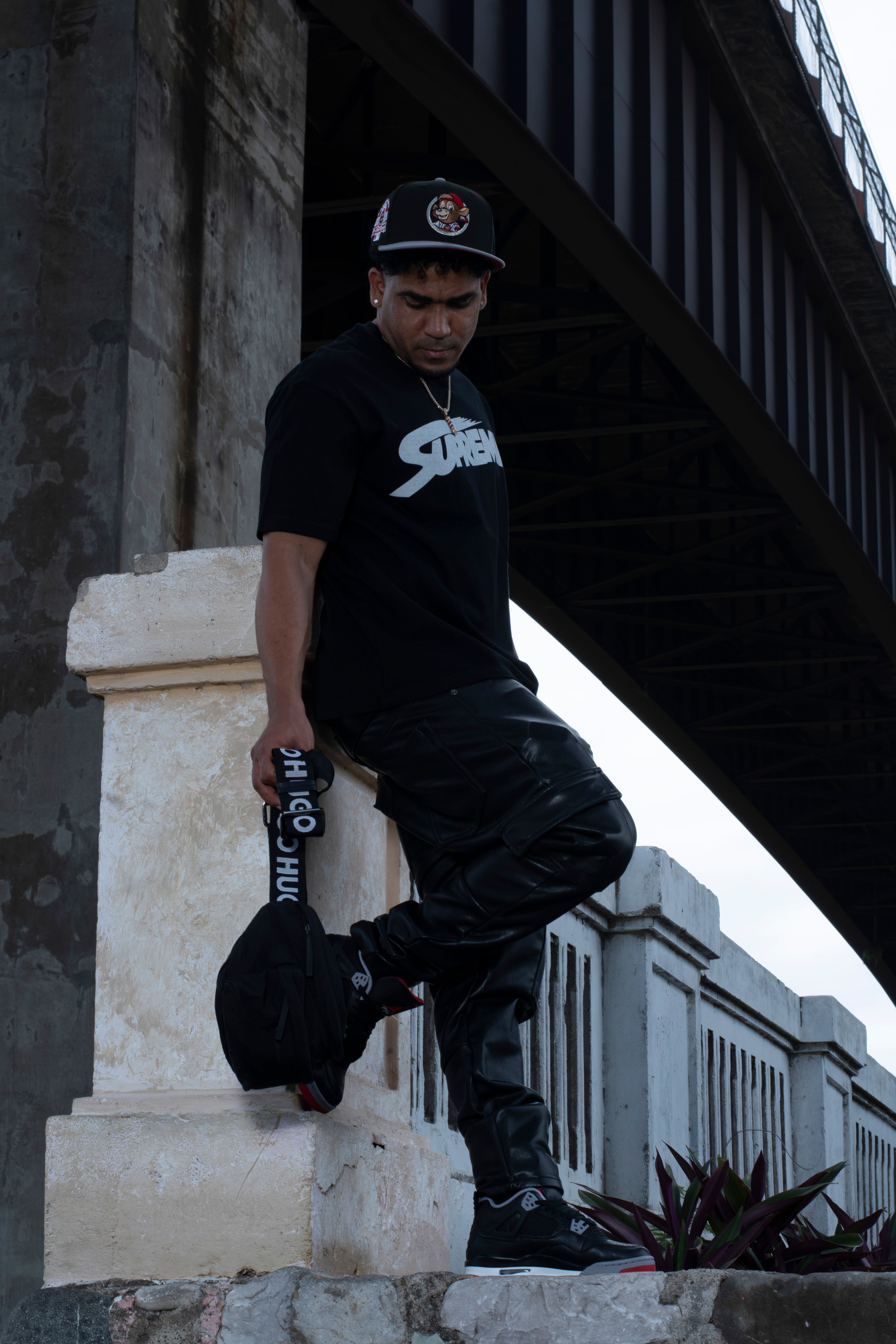 Cool urban portrait of a man leaning on a bridge rail, wearing streetwear.