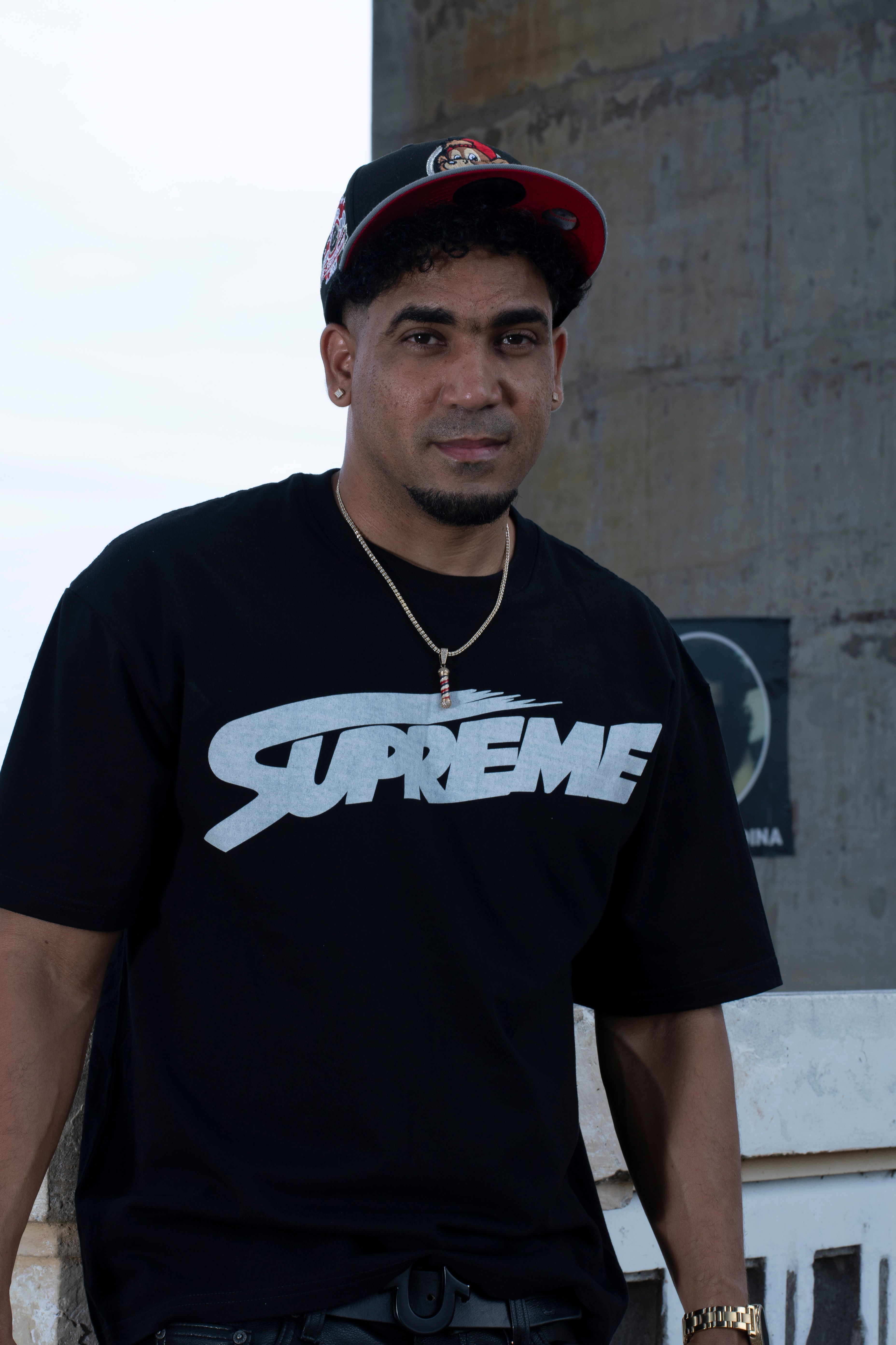 Urban portrait of a man wearing a Supreme t-shirt and cap, standing outdoors.