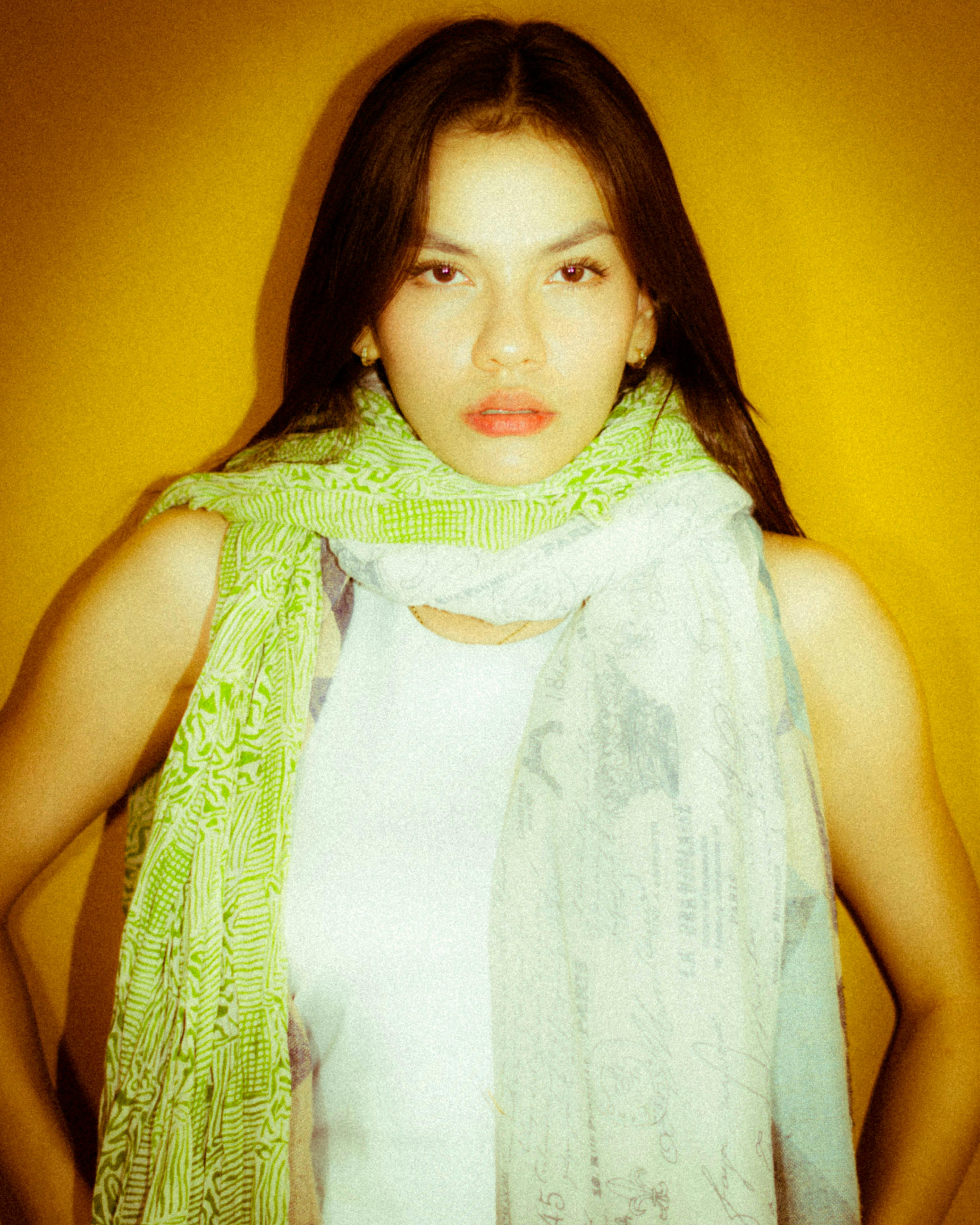 Woman poses with vibrant scarves against bright yellow backdrop in a modern portrait.