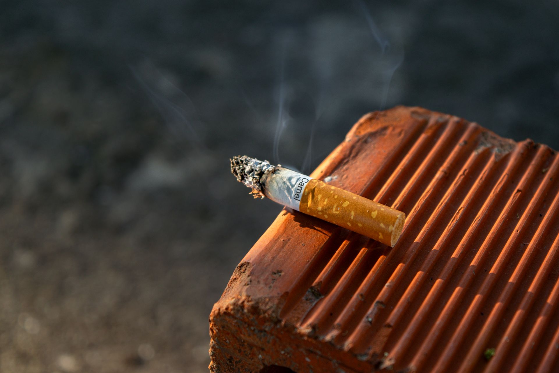 Close-up of a smoked cigarette butt resting on a textured clay surface in outdoor light.