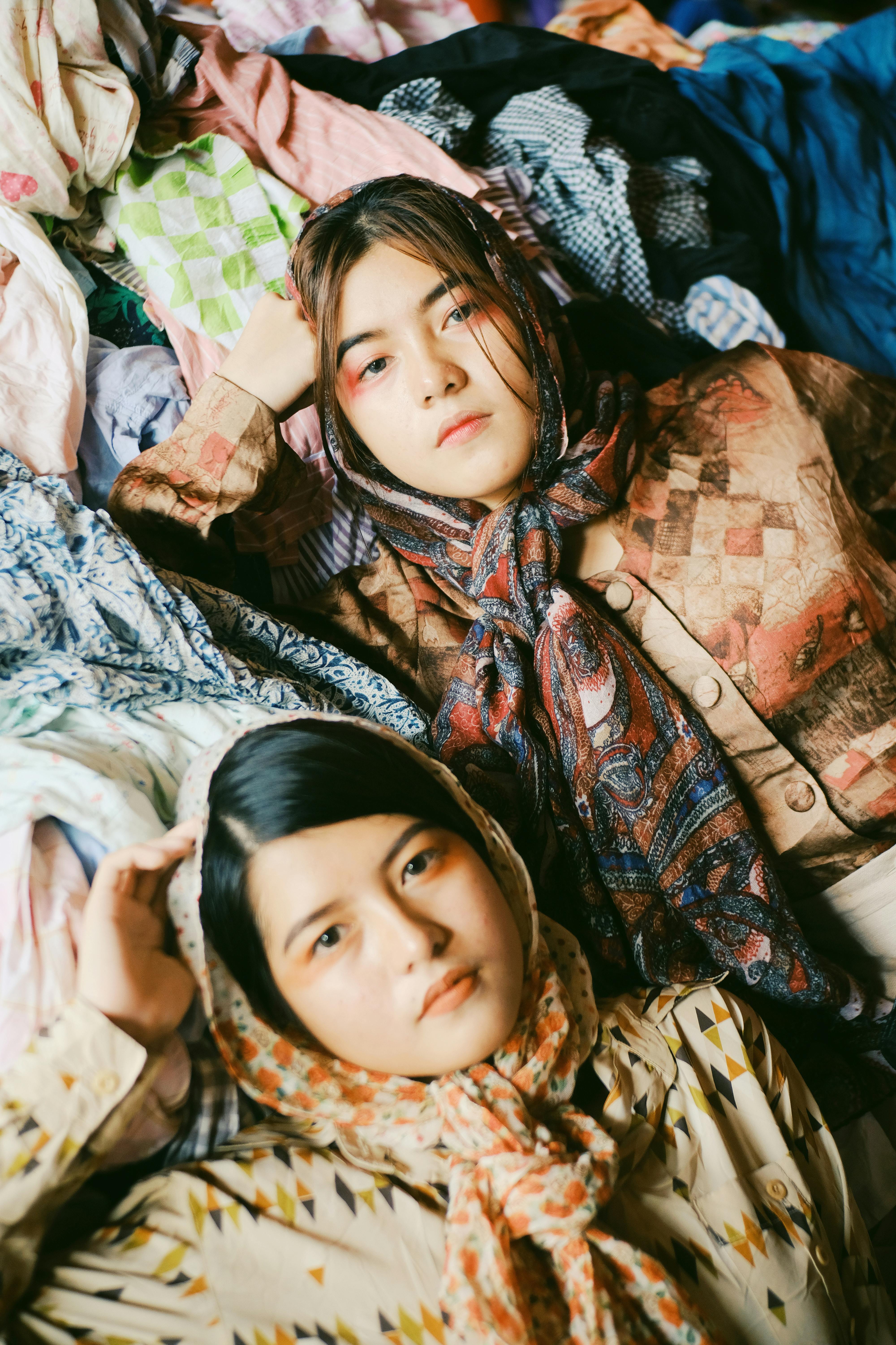 两名围着鲜艳围巾的妇女在色彩缤纷的室内纺织品前摆姿势，突出时尚与风格