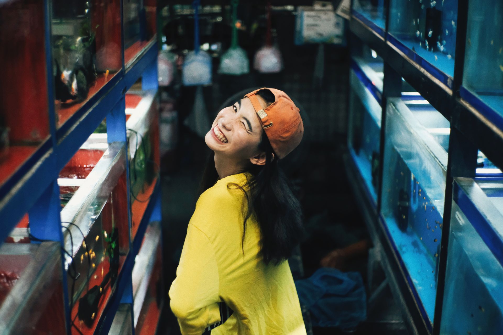 A cheerful woman in casual attire smiles while standing in a lively aquarium shop.