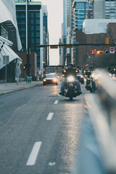Motorcyclists cruising down a bustling city street surrounded by skyscrapers.