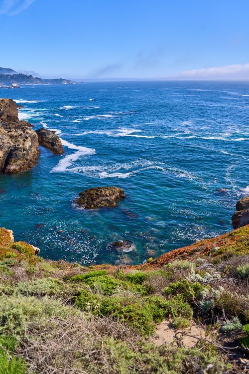 Free Breathtaking view of blue ocean waves hitting rocky cliffs on a sunny day. Stock Photo