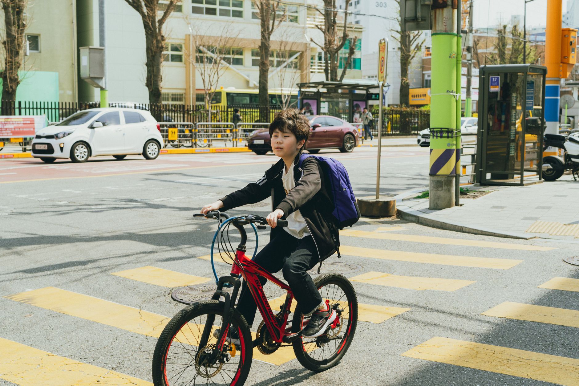 A young boy rides a bicycle across a crosswalk in bustling Seoul, South Korea.