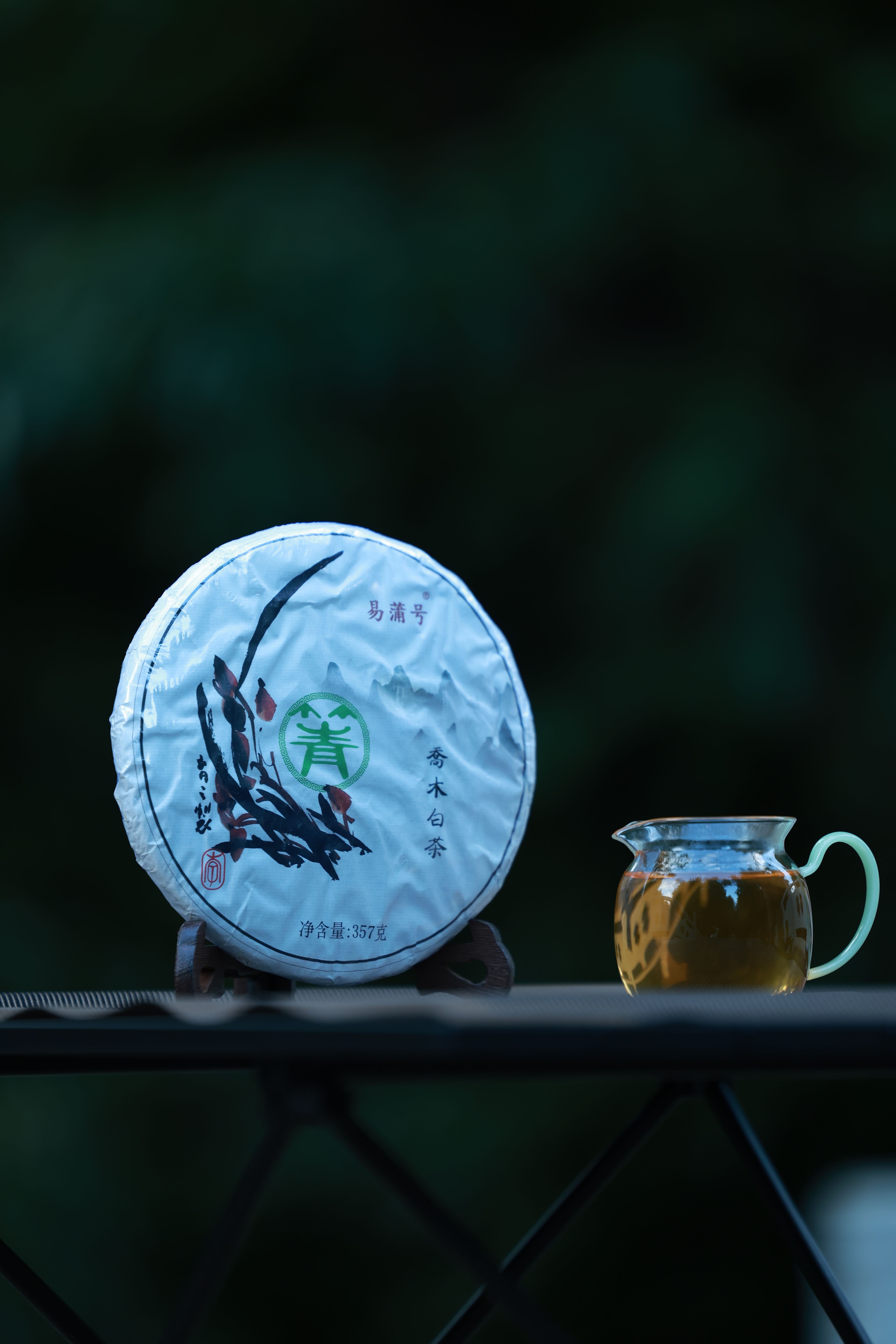 Dark, coiled pu-erh tea leaves steeping in a white porcelain gaiwan next to two small cups of reddish-brown brewed tea.