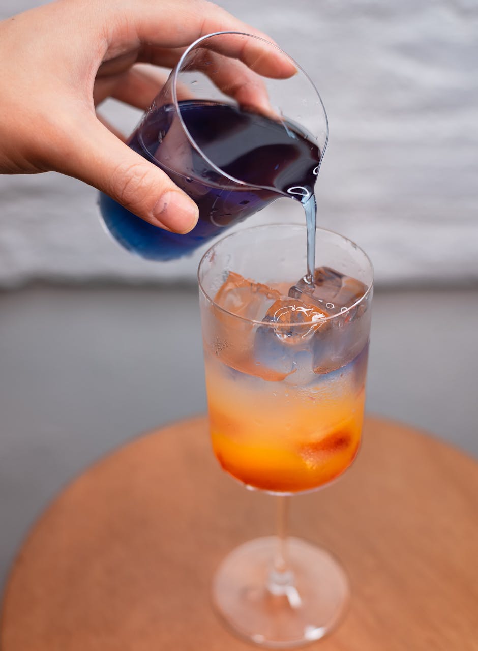 A colorful cocktail being poured in a glass, showcasing vibrant layers and ice cubes in Shinjuku, Tokyo.