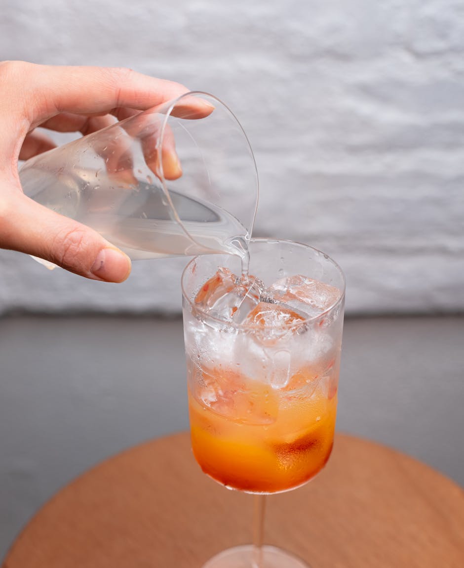 A vibrant citrus cocktail with ice being poured in a clear glass, offering a refreshing drink option.