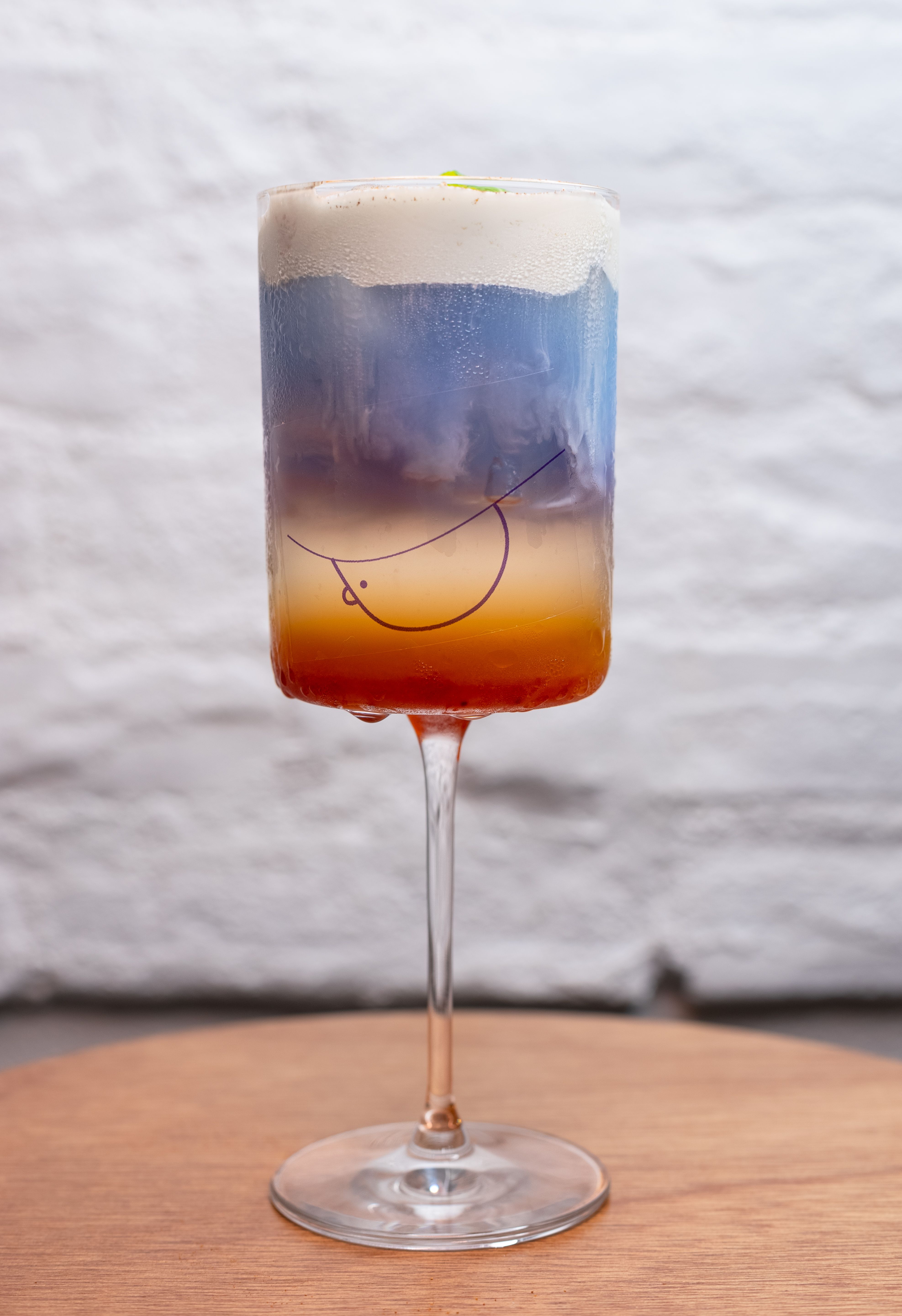 A visually stunning layered cocktail in a stylish wine glass against a textured wall.