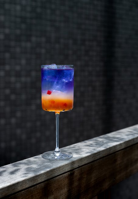 Vibrant cocktail with layers of color, ice, and fruit garnish served in a tall glass.