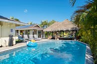 这是一个宁静的热带度假胜地，拥有一个被郁郁葱葱的绿植和茅草屋环绕的游泳池