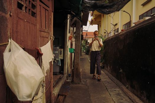 A man uses his smartphone while walking through a narrow alley in Bangkok, Thailand.