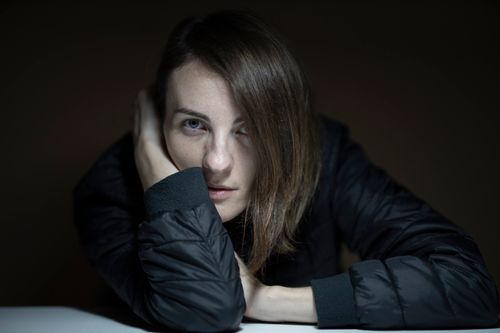 Free Close-up portrait of a young woman in a dark setting wearing a jacket, looking thoughtfully into the camera. Stock Photo