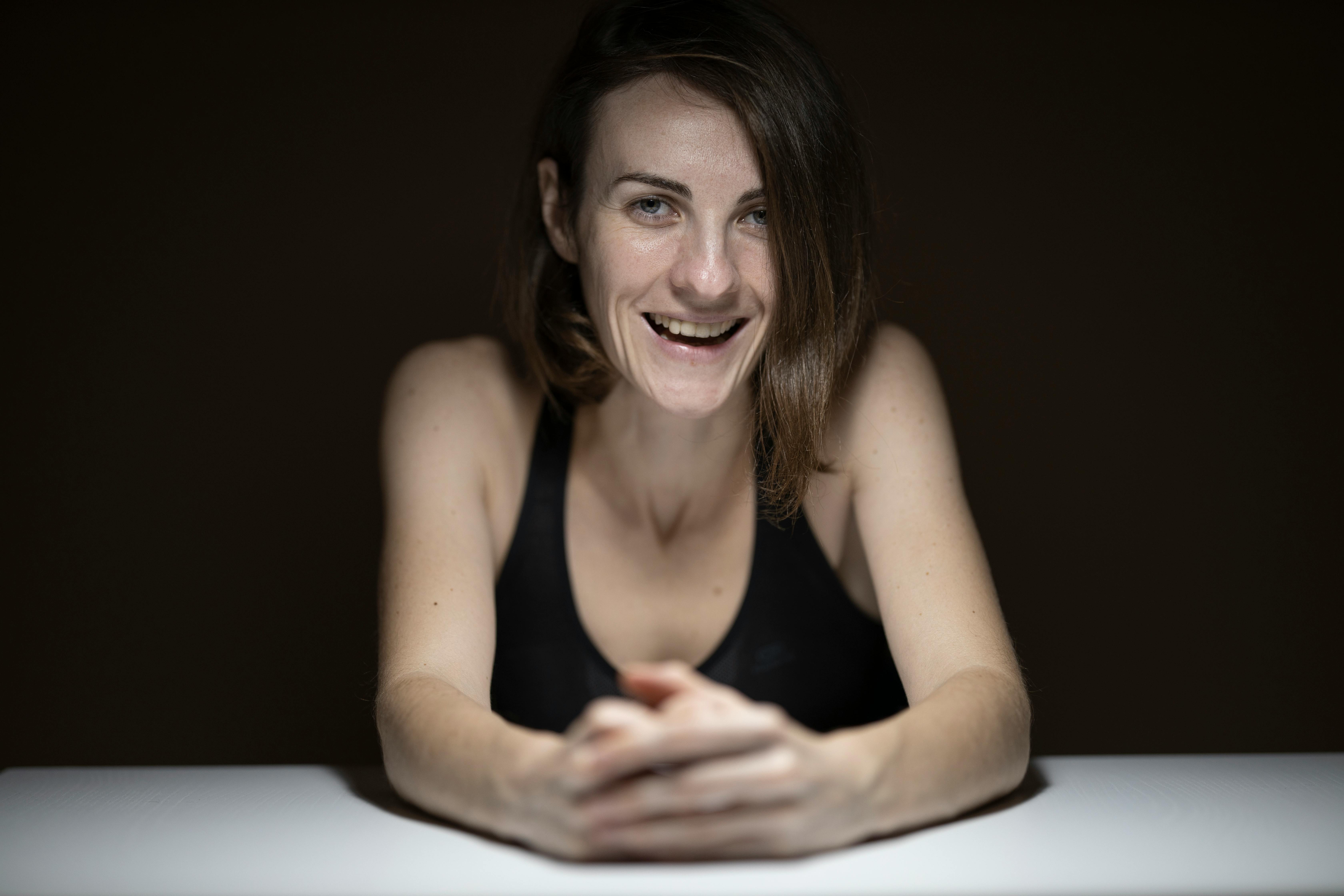 Portrait of a smiling woman in a dark setting, leaning on a table, exuding warmth and confidence.