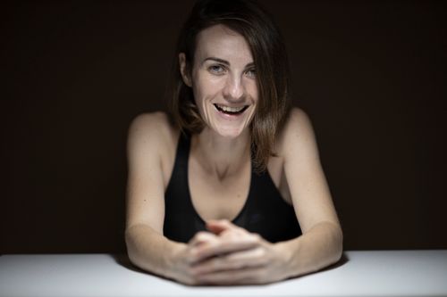Free Portrait of a smiling woman in a dark setting, leaning on a table, exuding warmth and confidence. Stock Photo