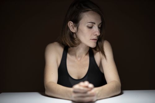 Free A contemplative woman looking down, captured in a soft, moody light indoors. Stock Photo