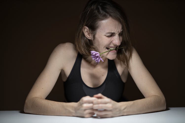 Woman In Black Tank Top Biting Purple Petaled Flower