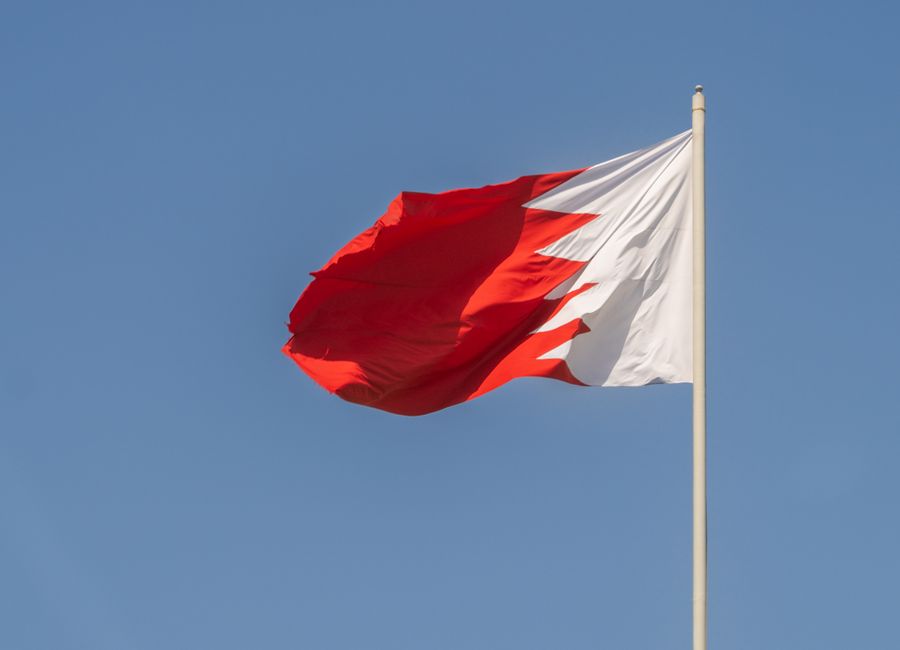 Bahraini national flag waving prominently against a clear blue sky, symbolizing national pride.