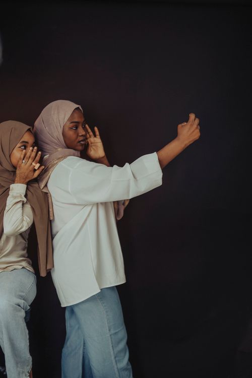 Free Two women in hijabs taking a selfie with a phone against a dark backdrop. Stock Photo