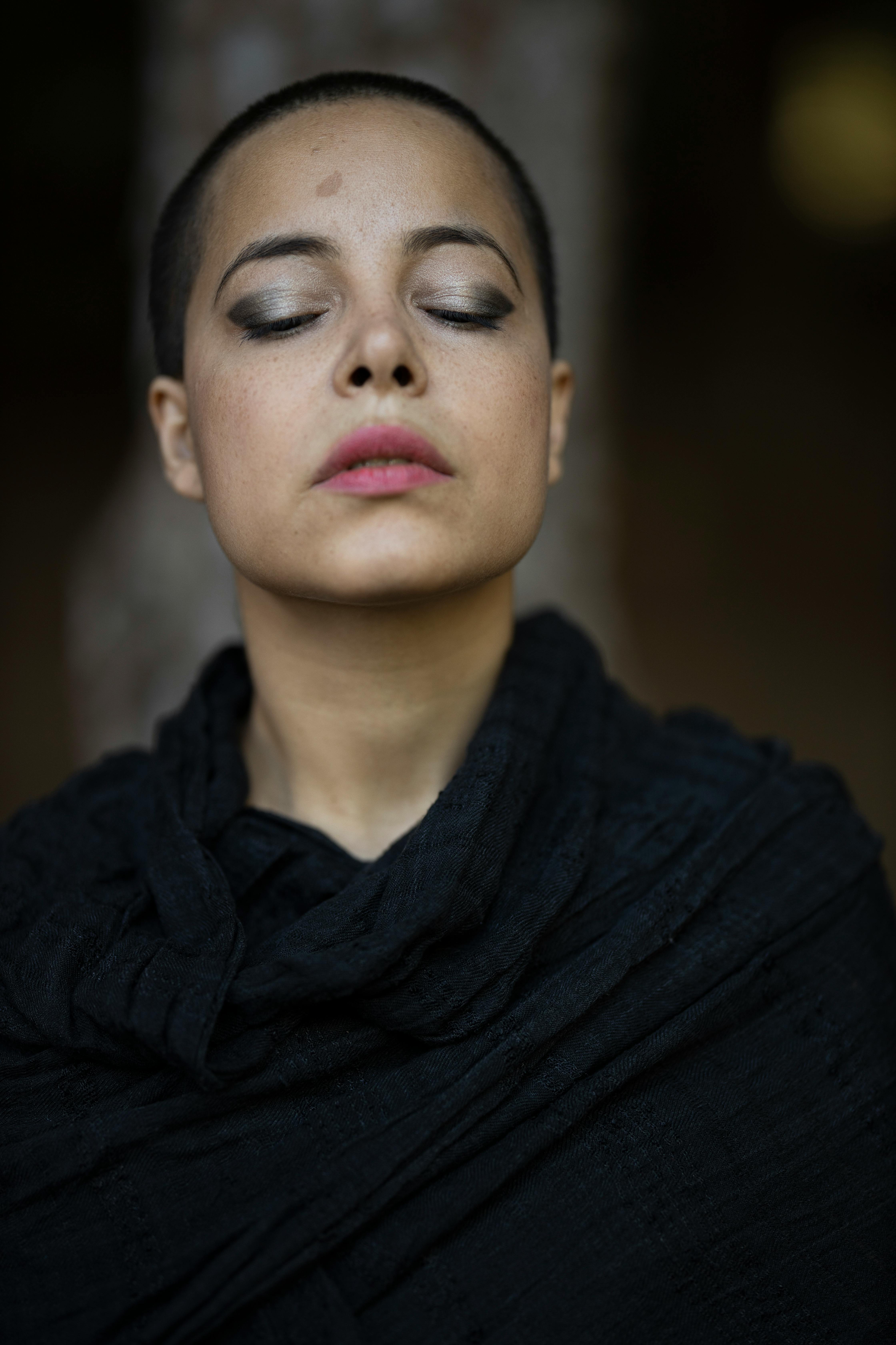 一位闭着眼睛、妆容时尚、身着深色包裹的女性宁静肖像