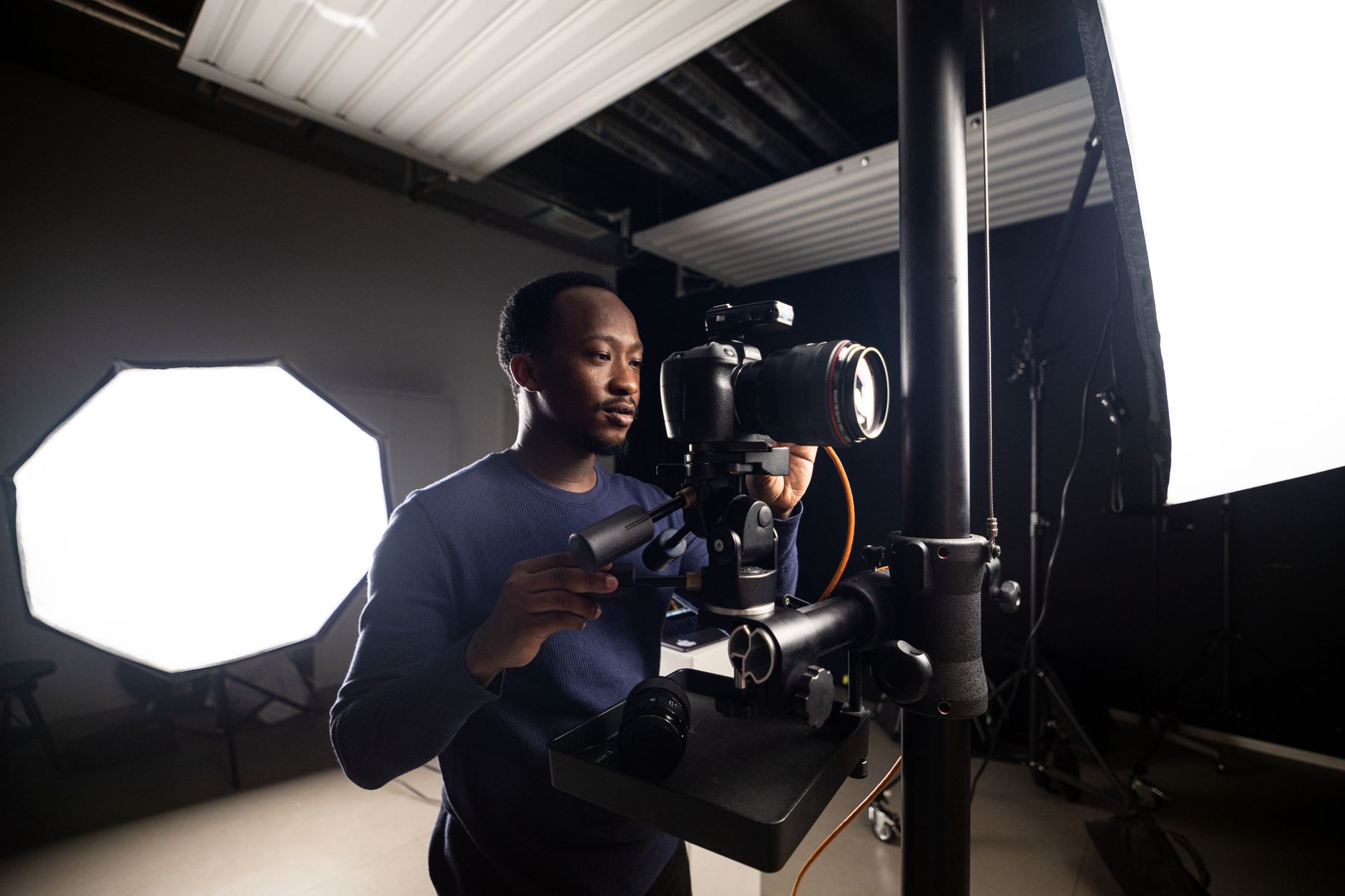 Photographer adjusting camera in studio, surrounded by lighting equipment.