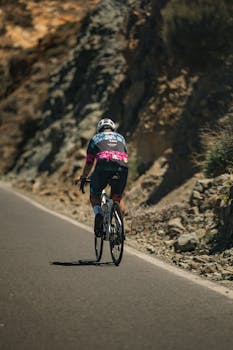 Cyclist in sports gear rides up a mountain road, showcasing endurance and scenic views.
