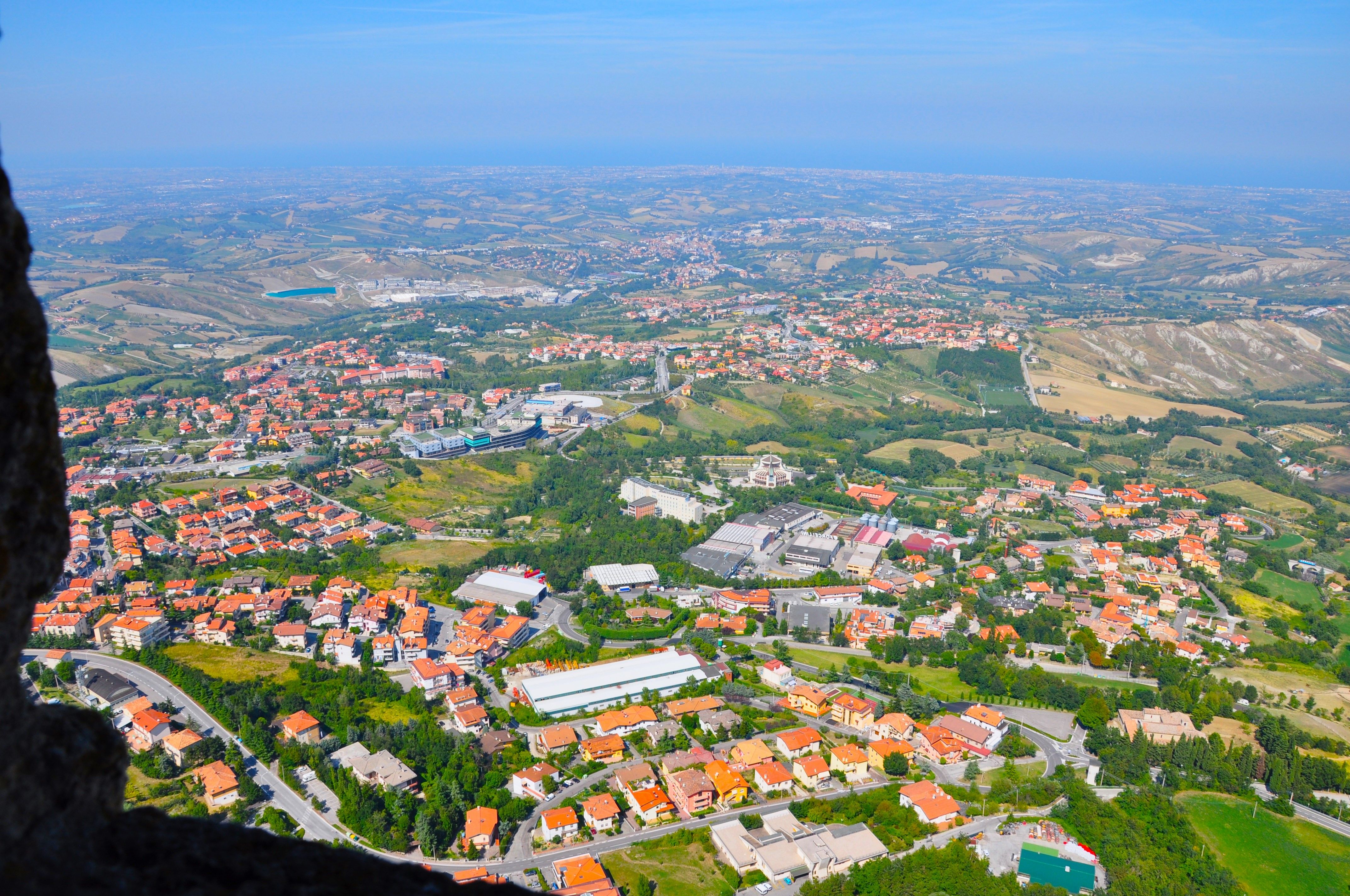 Discover the scenic aerial view of San Marino with vibrant red rooftops and lush green fields.